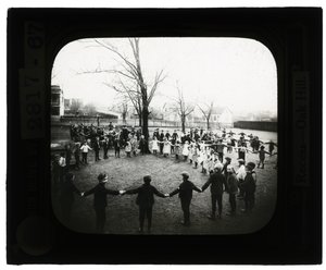 Foto horizontal en blanco y negro de niños y niñas tomados de la mano formando círculos al aire libre